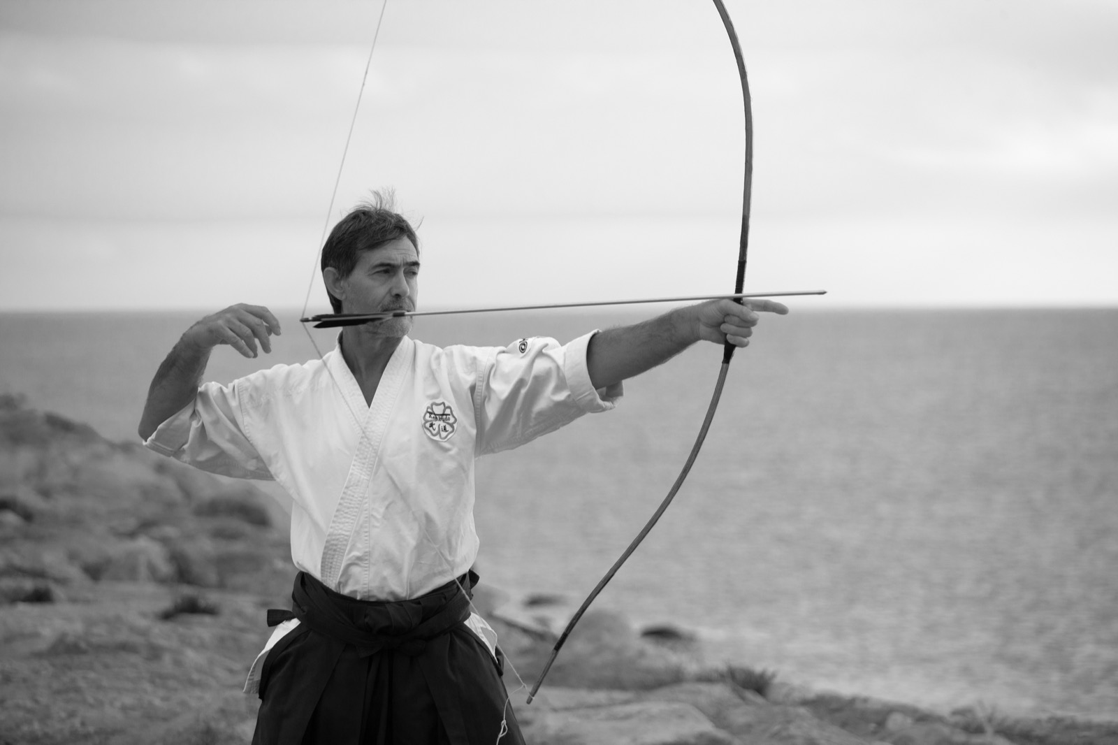 Un arquero practica kyudo junto al mar, fotografía en blanco y negro
