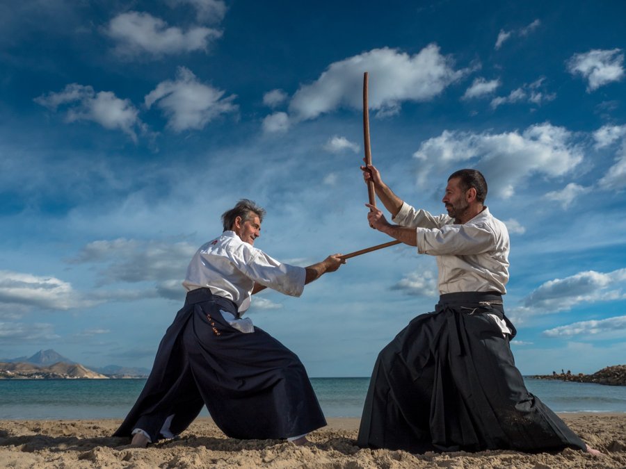 Dos practicantes con espadas de madera en la playa