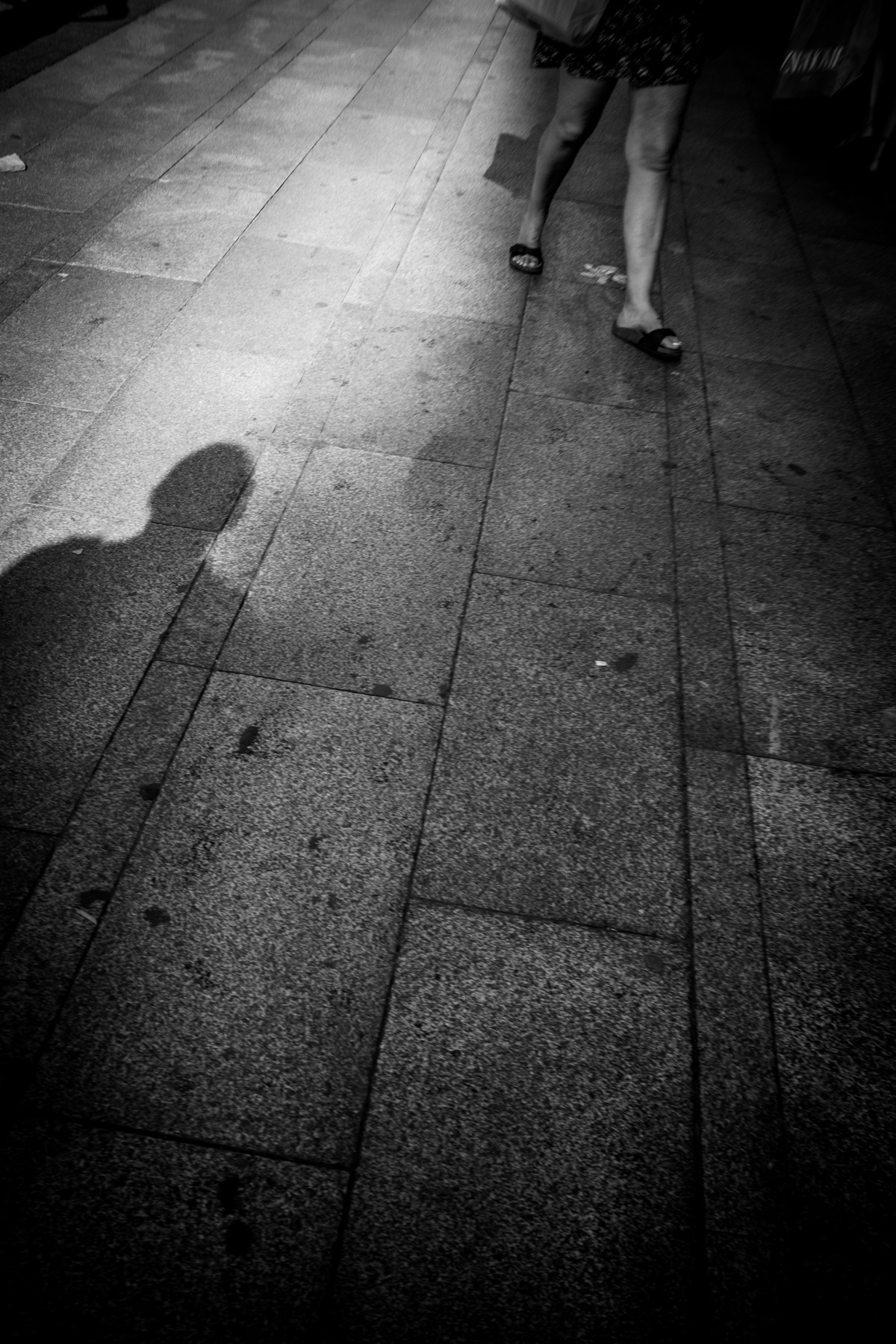 Fotografía en blanco y negro de una sombra y una persona caminando sobre la acera